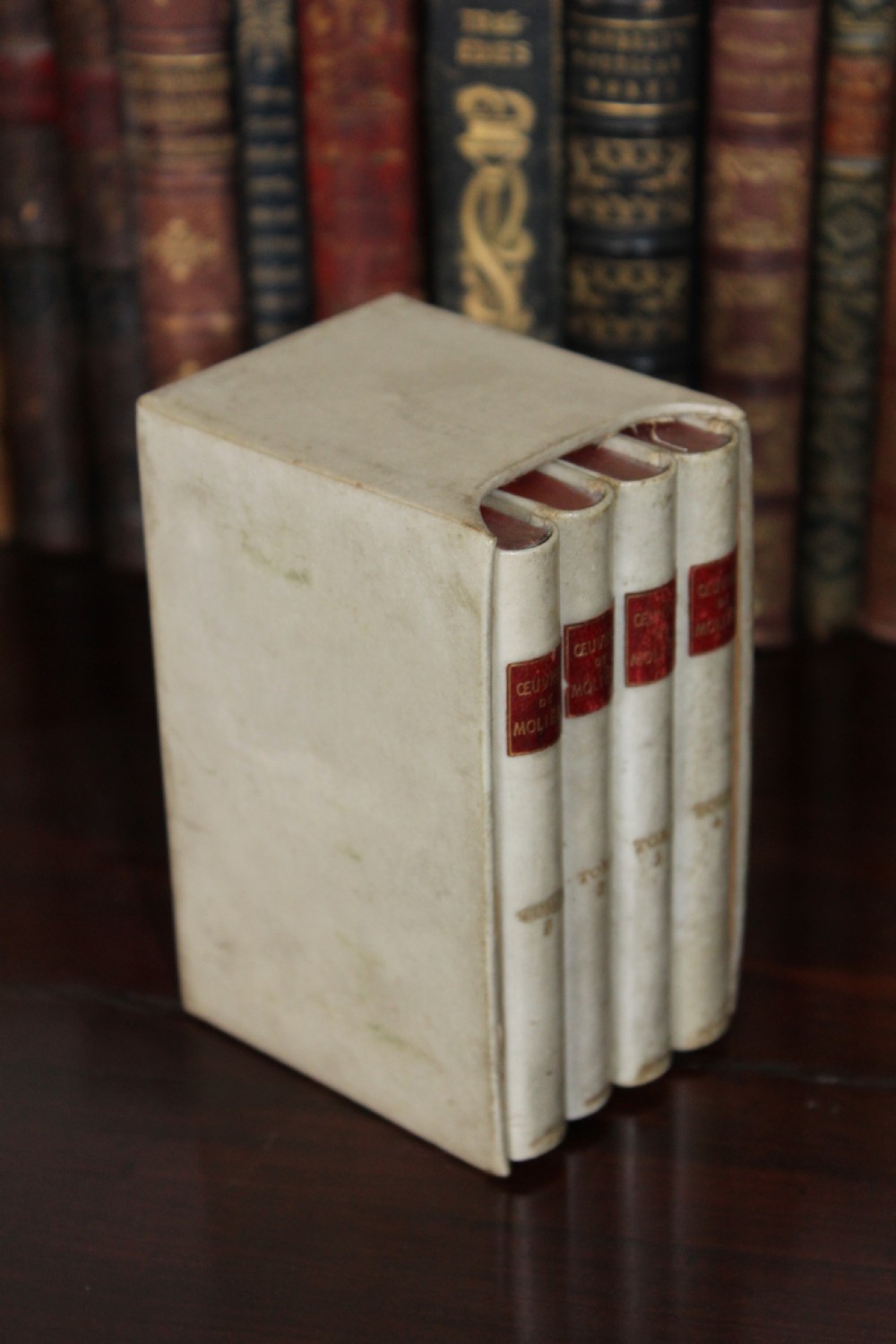 A four-volume set of small antique books bound in cream vellum with red gilt-tooled spine labels, housed inside a matching vellum slipcase. View III