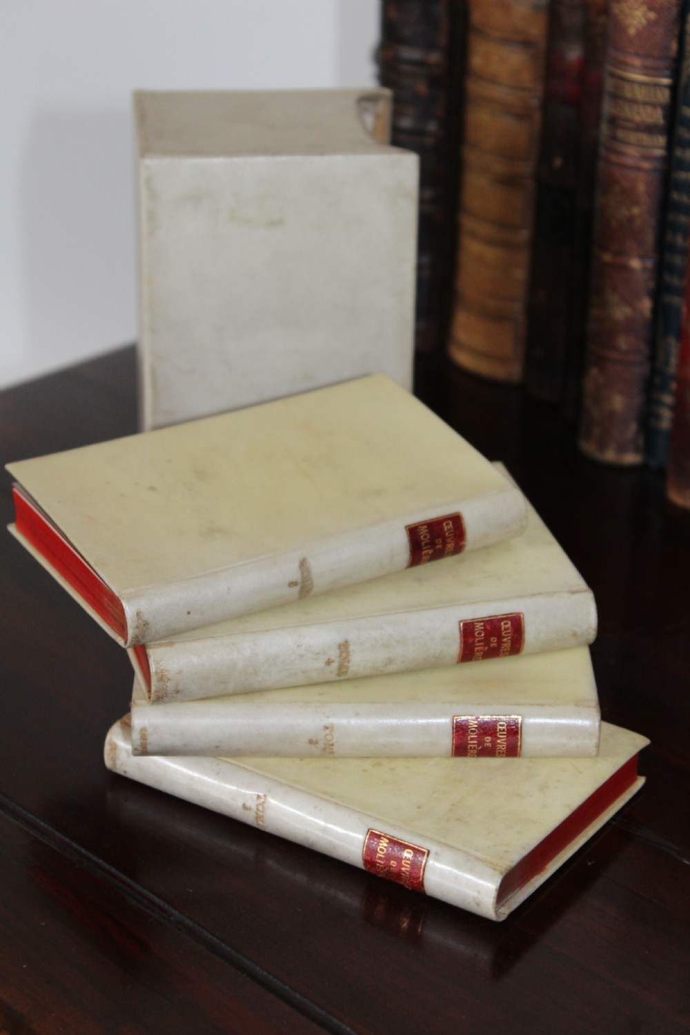 A four-volume set of small antique books bound in cream vellum with red gilt-tooled spine labels, housed inside a matching vellum slipcase. View IV