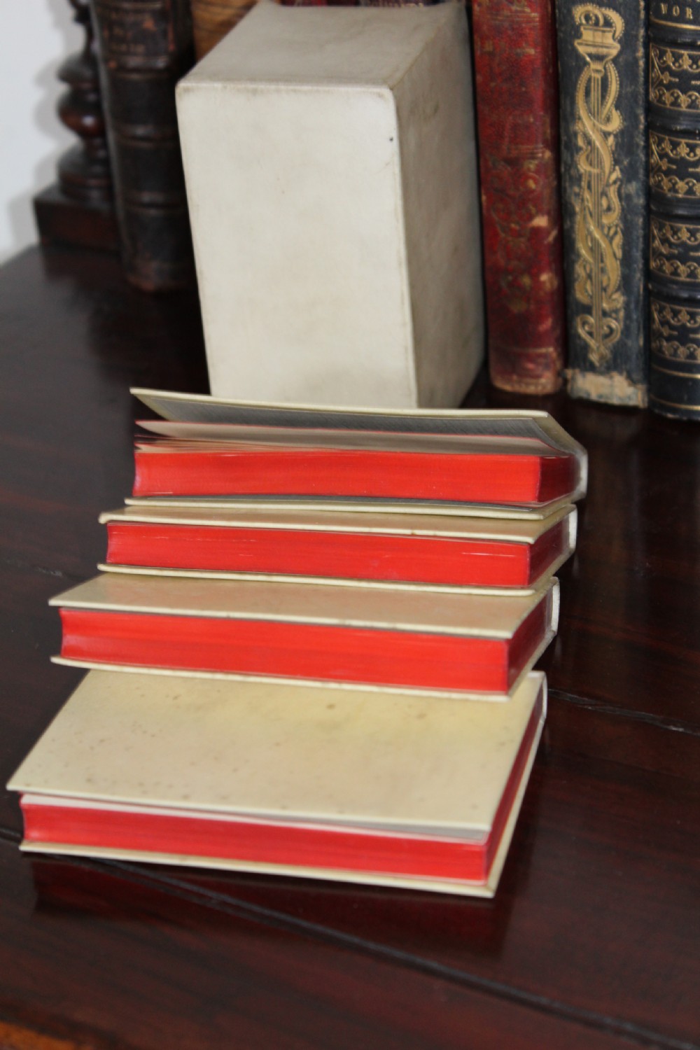 A four-volume set of small antique books bound in cream vellum with red gilt-tooled spine labels, housed inside a matching vellum slipcase. View V