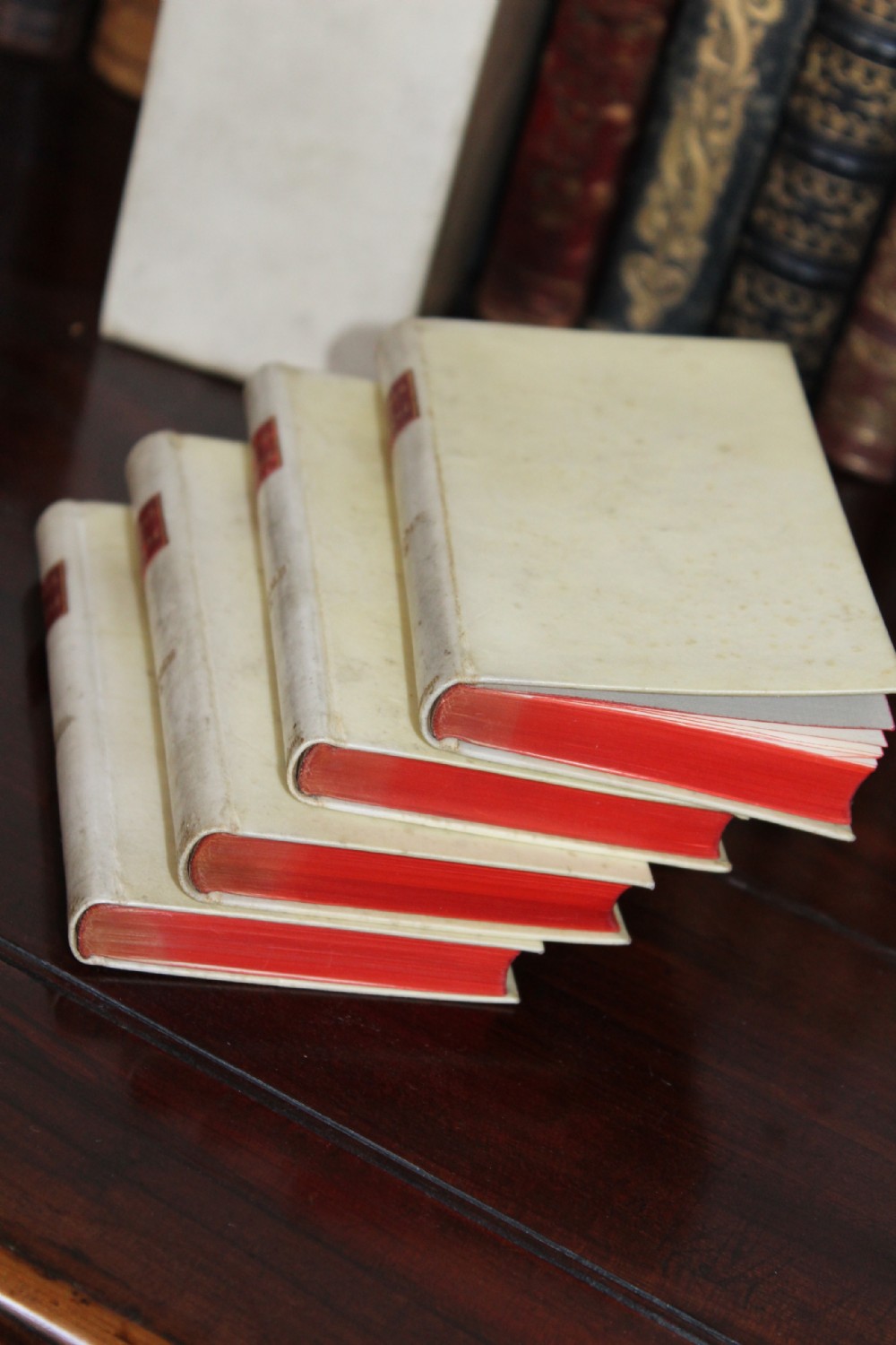 A four-volume set of small antique books bound in cream vellum with red gilt-tooled spine labels, housed inside a matching vellum slipcase. View VI