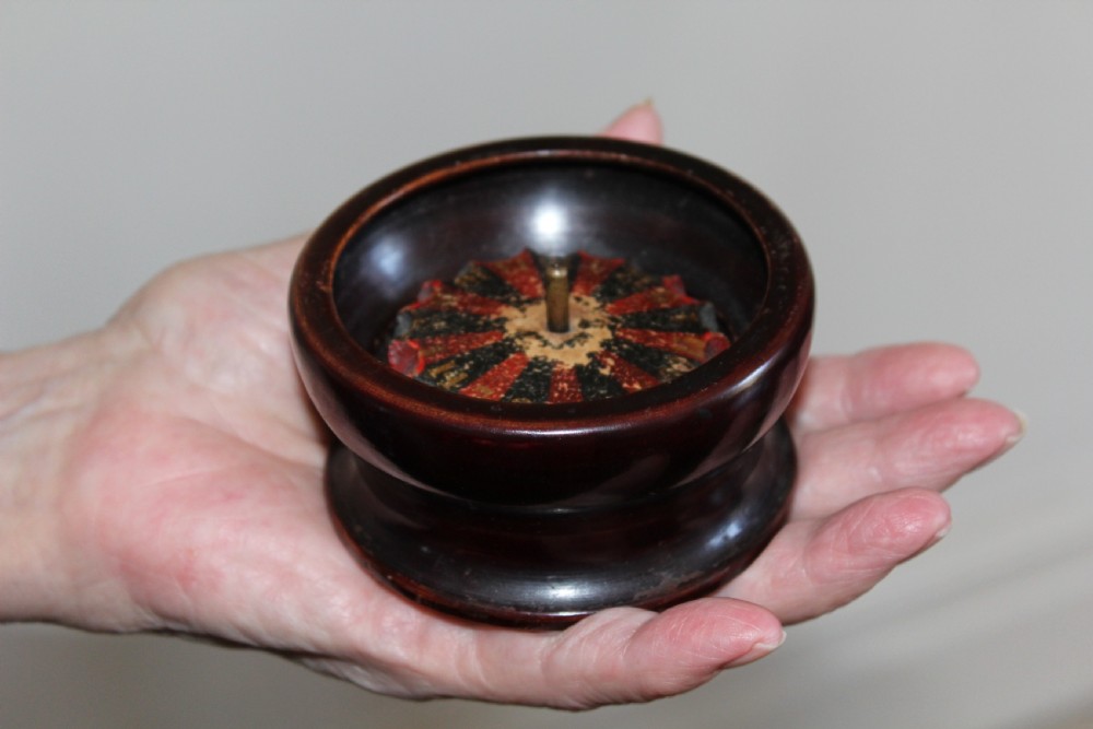 A compact, turned dark wood miniature travelling roulette wheel featuring red and black numbered segments around a central brass spindle.