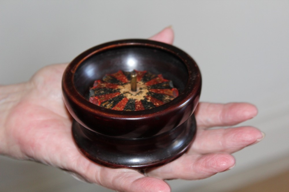 A compact, turned dark wood miniature travelling roulette wheel featuring red and black numbered segments around a central brass spindle. View II