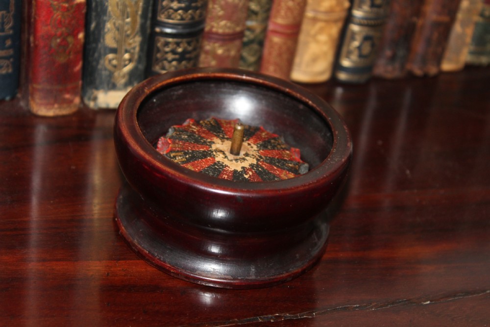 A compact, turned dark wood miniature travelling roulette wheel featuring red and black numbered segments around a central brass spindle. View III