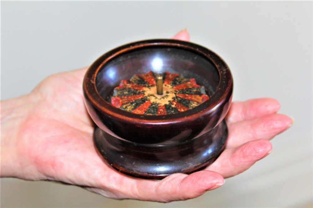 A compact, turned dark wood miniature travelling roulette wheel featuring red and black numbered segments around a central brass spindle. View VII