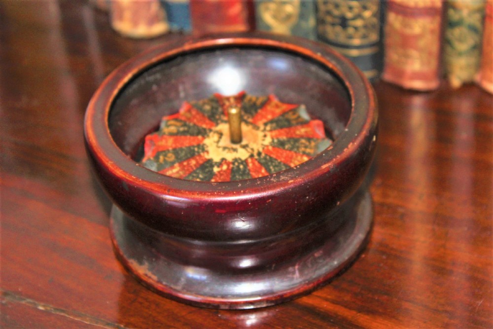 A compact, turned dark wood miniature travelling roulette wheel featuring red and black numbered segments around a central brass spindle. View VIII