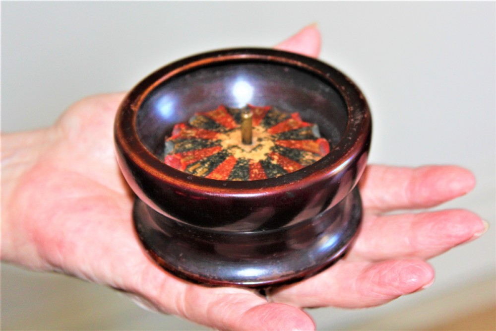 A compact, turned dark wood miniature travelling roulette wheel featuring red and black numbered segments around a central brass spindle. View IX