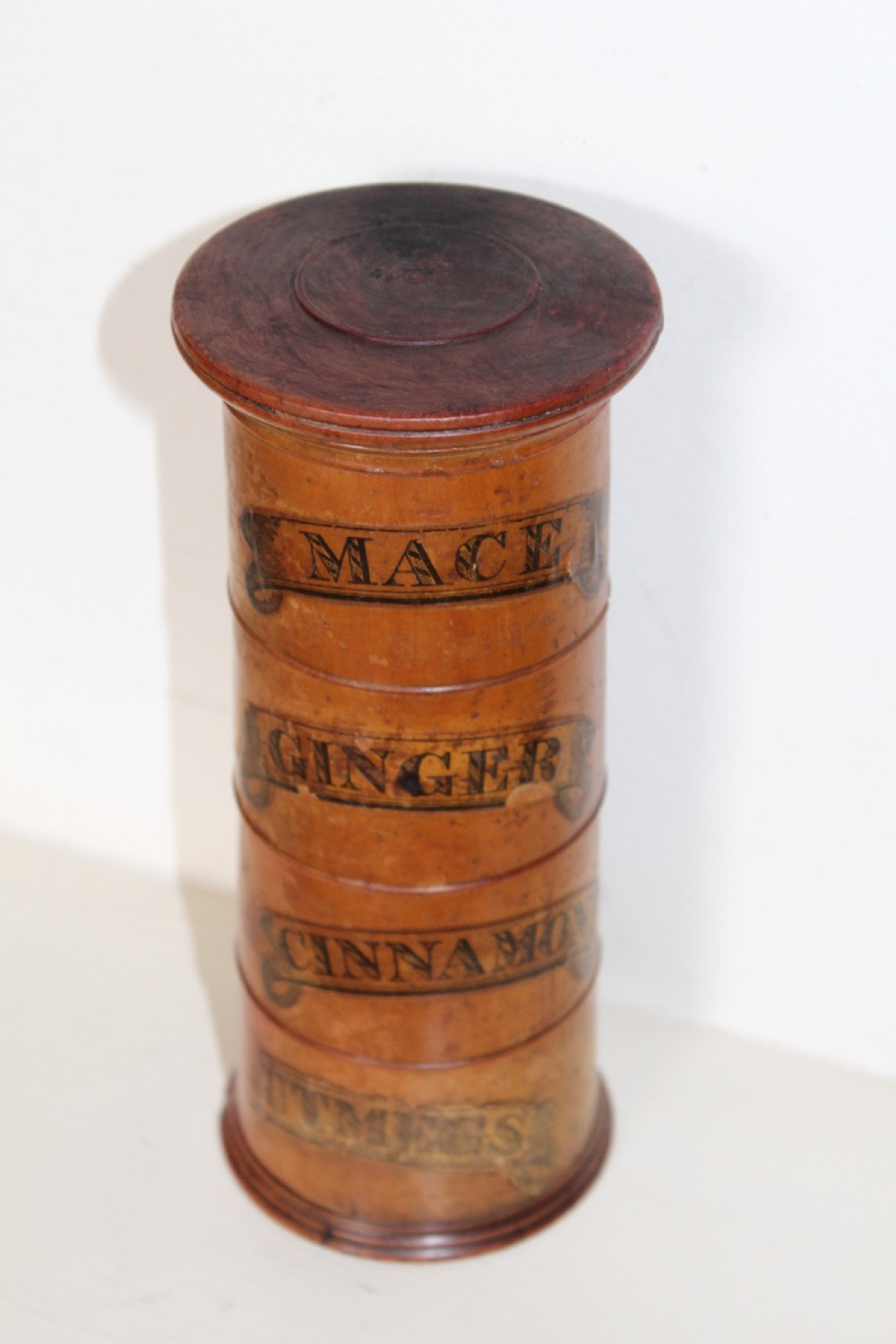 A turned wooden four-tier cylindrical spice tower with paper label banners marking Mace, Ginger, Cinnamon, and Nutmegs. View II