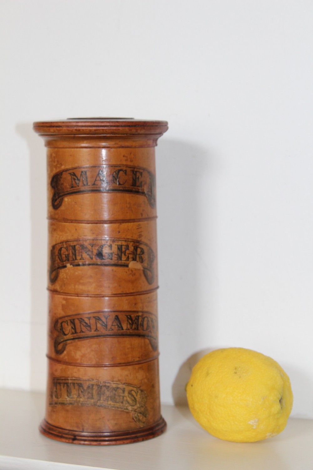 A turned wooden four-tier cylindrical spice tower with paper label banners marking Mace, Ginger, Cinnamon, and Nutmegs. View III
