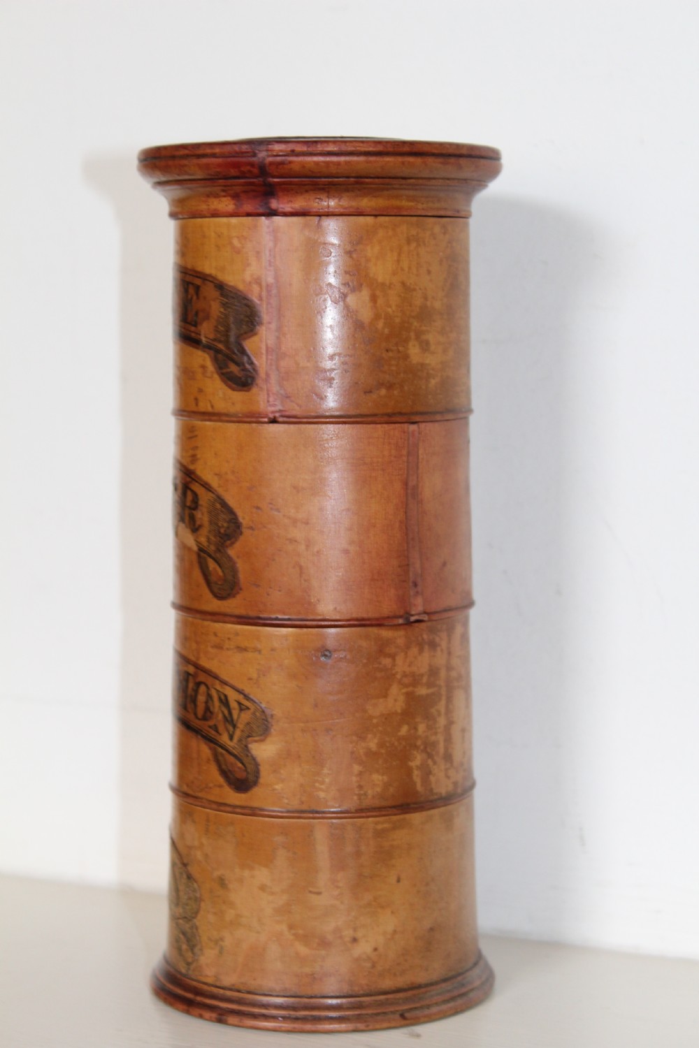 A turned wooden four-tier cylindrical spice tower with paper label banners marking Mace, Ginger, Cinnamon, and Nutmegs. View VII