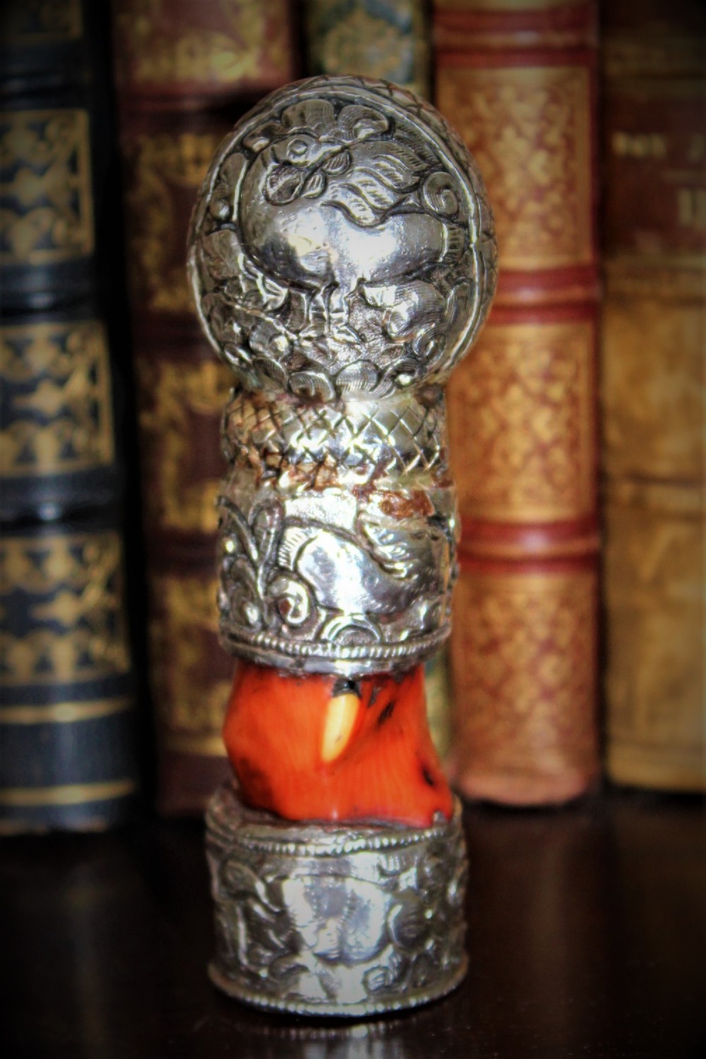 An ornate Middle Eastern desk seal crafted from chased silver with a section of natural red coral incorporated into the handle.