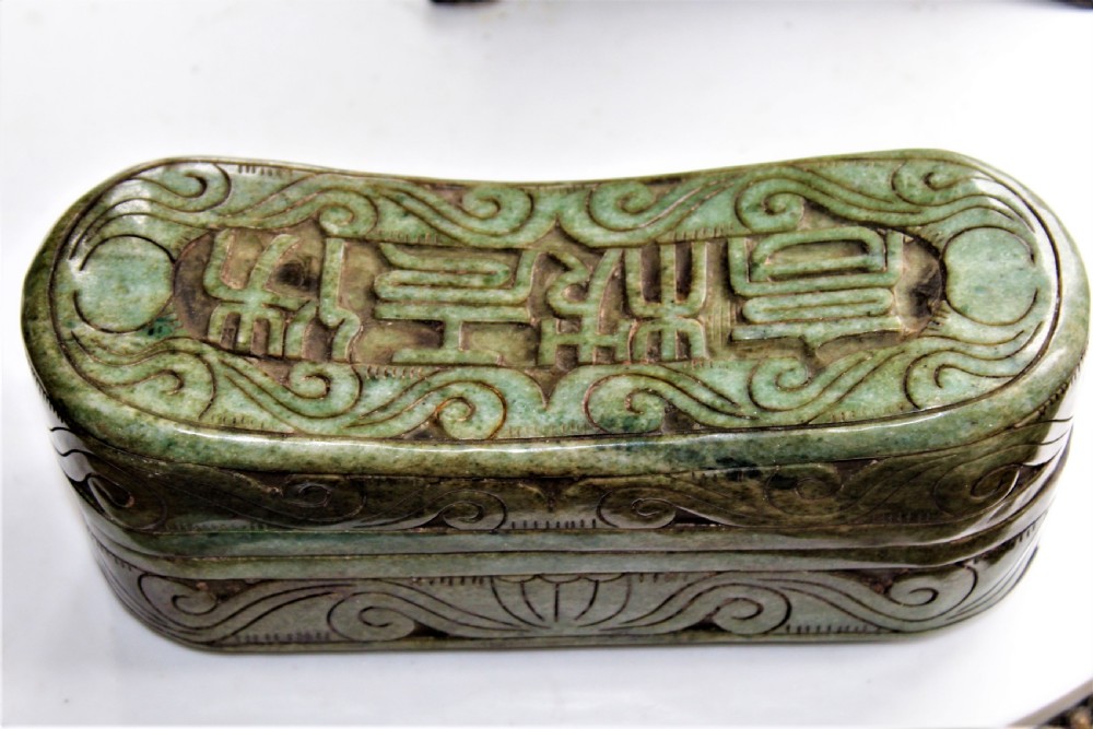 A carved light green hardstone Chinese pillow box with decorative scrollwork and carved characters on the concave upper surface.