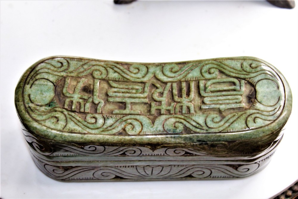 A carved light green hardstone Chinese pillow box with decorative scrollwork and carved characters on the concave upper surface. View II
