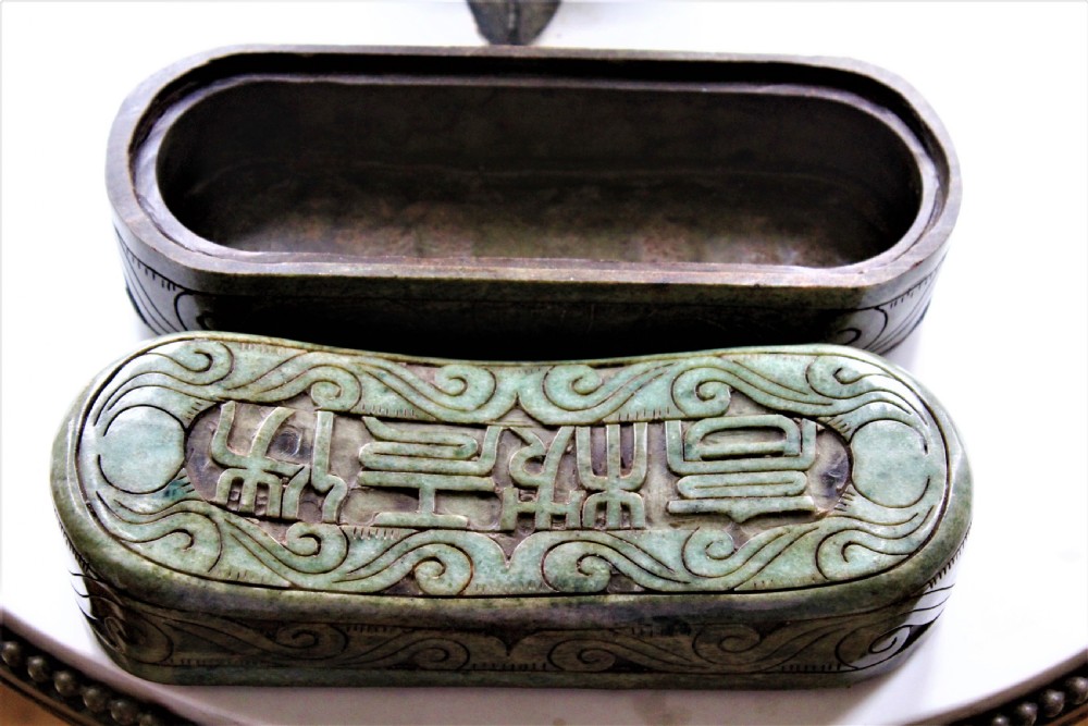 A carved light green hardstone Chinese pillow box with decorative scrollwork and carved characters on the concave upper surface. View VI
