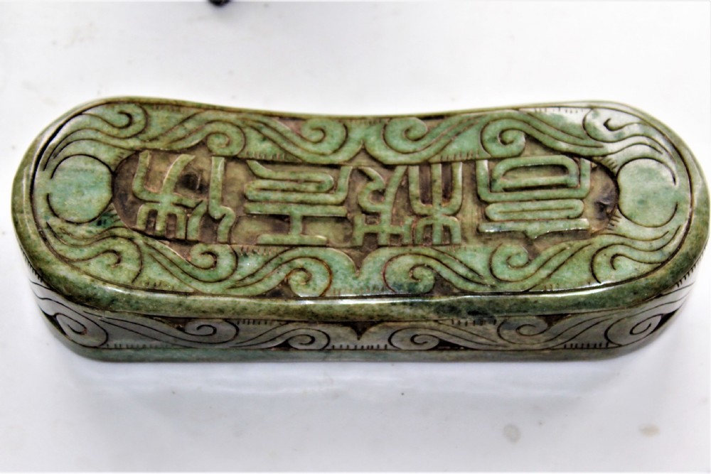 A carved light green hardstone Chinese pillow box with decorative scrollwork and carved characters on the concave upper surface. View VII