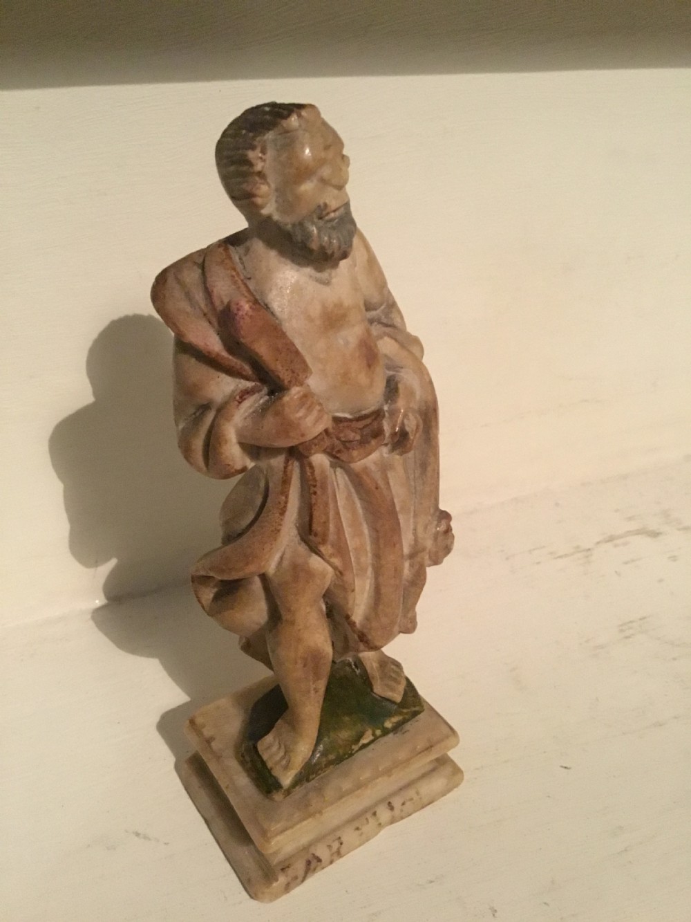 A carved beige marble figure depicting a bearded Roman philosopher in draped robes standing on a moulded plinth base. View II