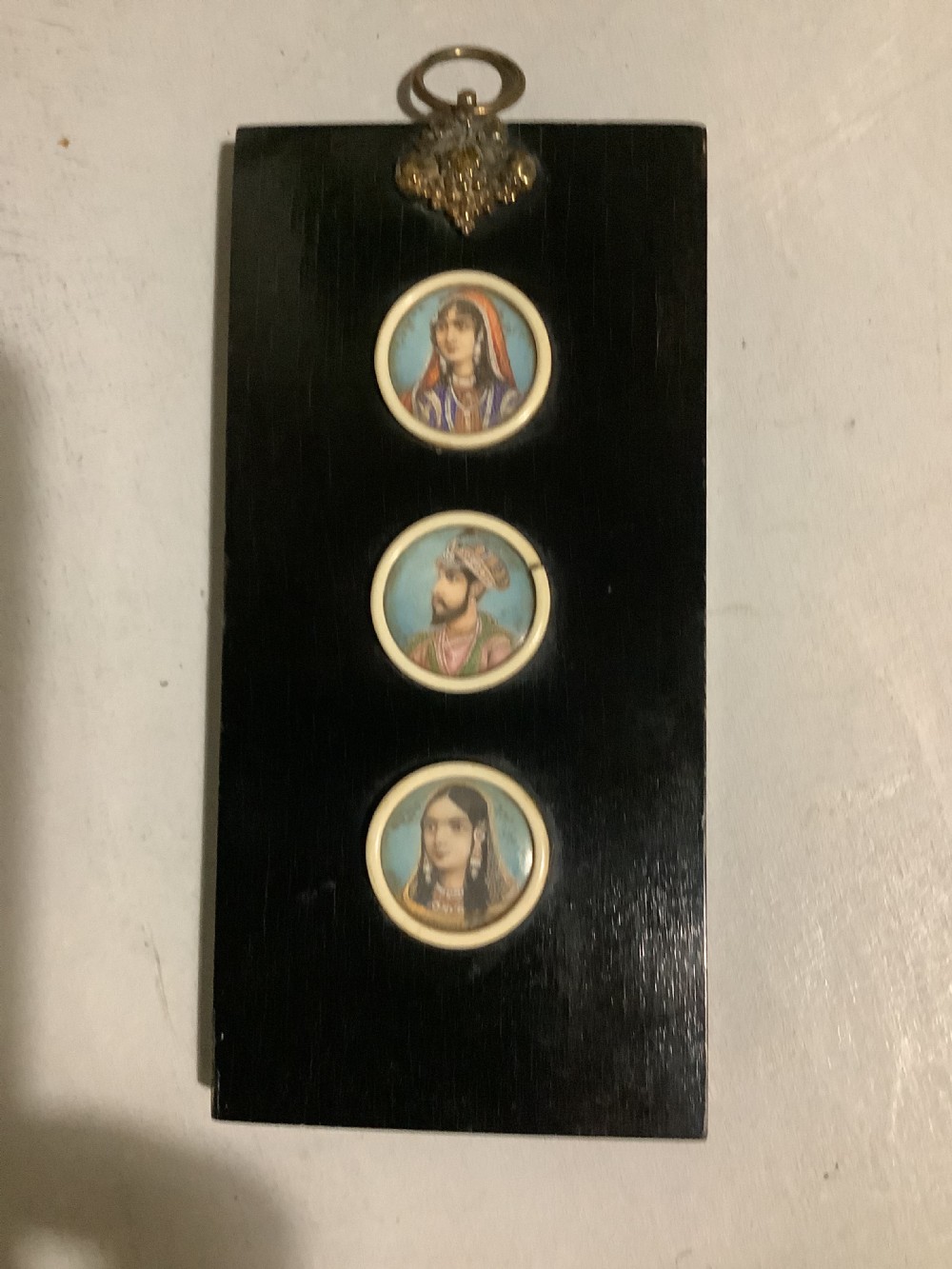 A small Indian ebonised wood painting of three miniatures finely painted on the back of the glass