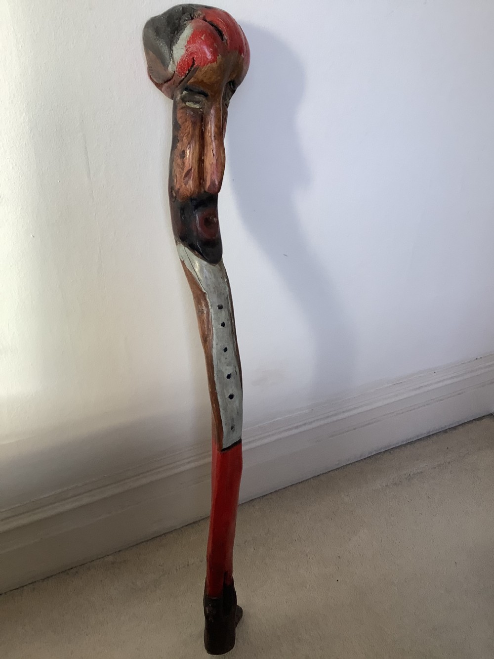 A hand-carved polychrome thorn wood walking stick featuring an anthropomorphic head and a painted red and grey shaft.
