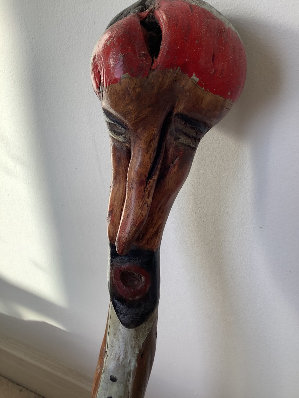 A hand-carved polychrome thorn wood walking stick featuring an anthropomorphic head and a painted red and grey shaft. View X