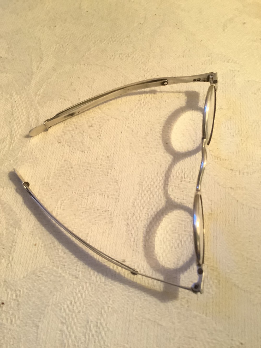 A pair of silver hallmarked folding spectacles positioned below a fitted tortoiseshell case with silver mounts. View II