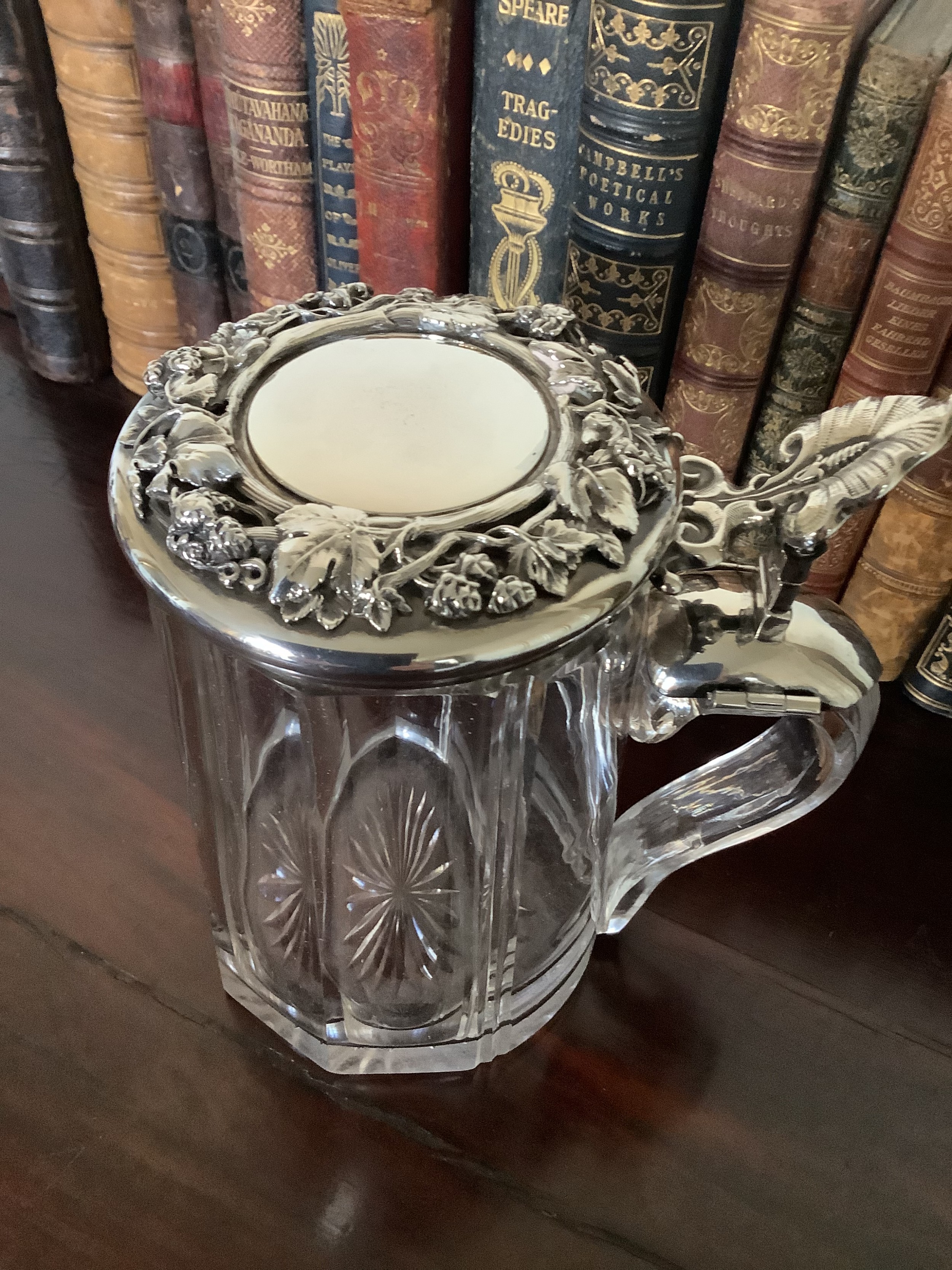 A 19th-century cut glass tankard featuring a clear glass handle and an embossed silver lid decorated with grapevine motifs.