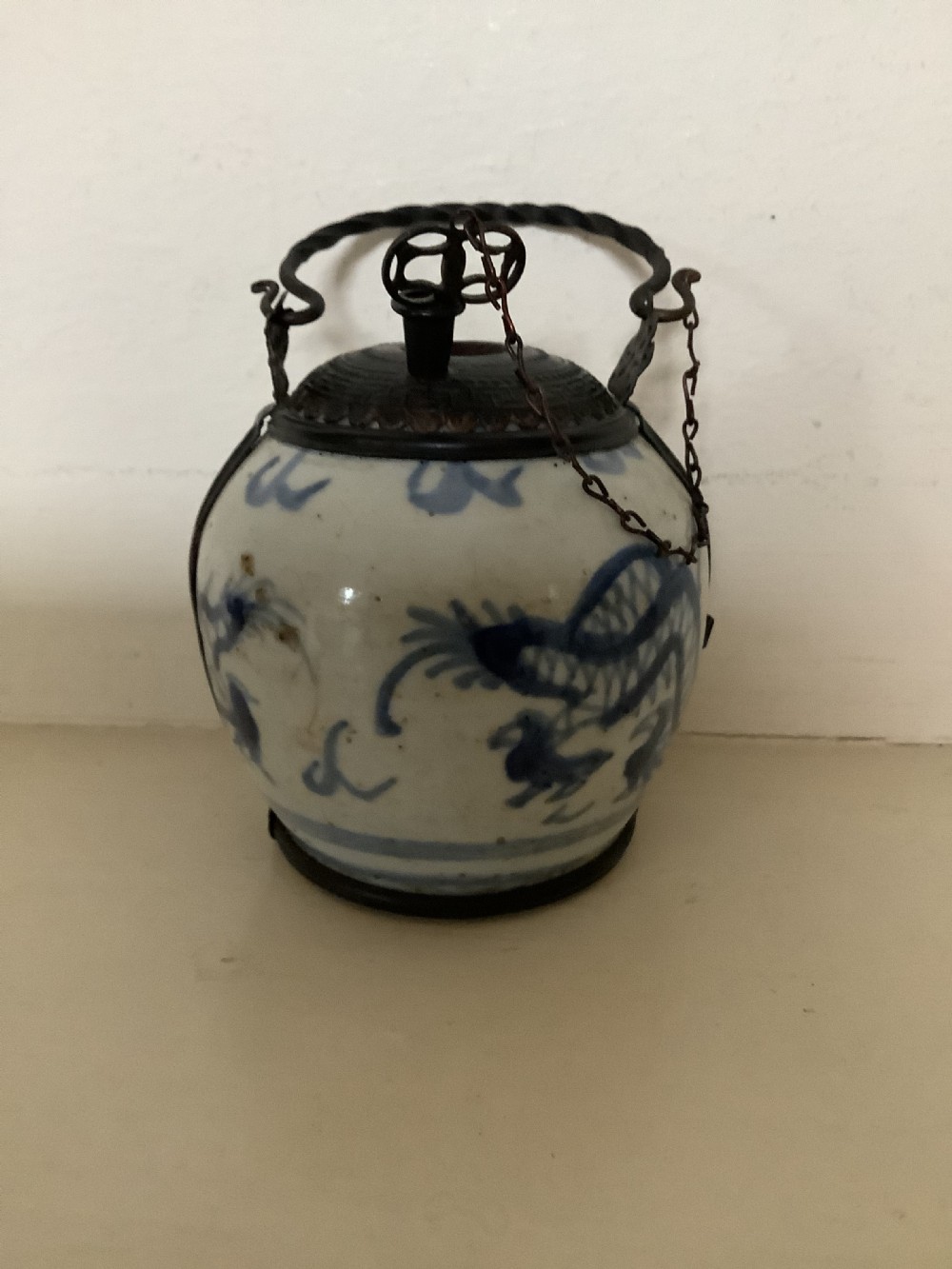 A small 19th-century Chinese blue and white porcelain pot featuring hand-painted motifs, enclosed in metal wire mounts with an attached stopper and handle.
