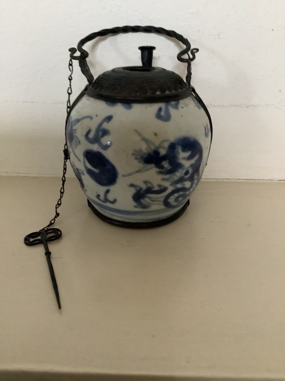 A small 19th-century Chinese blue and white porcelain pot featuring hand-painted motifs, enclosed in metal wire mounts with an attached stopper and handle. View II