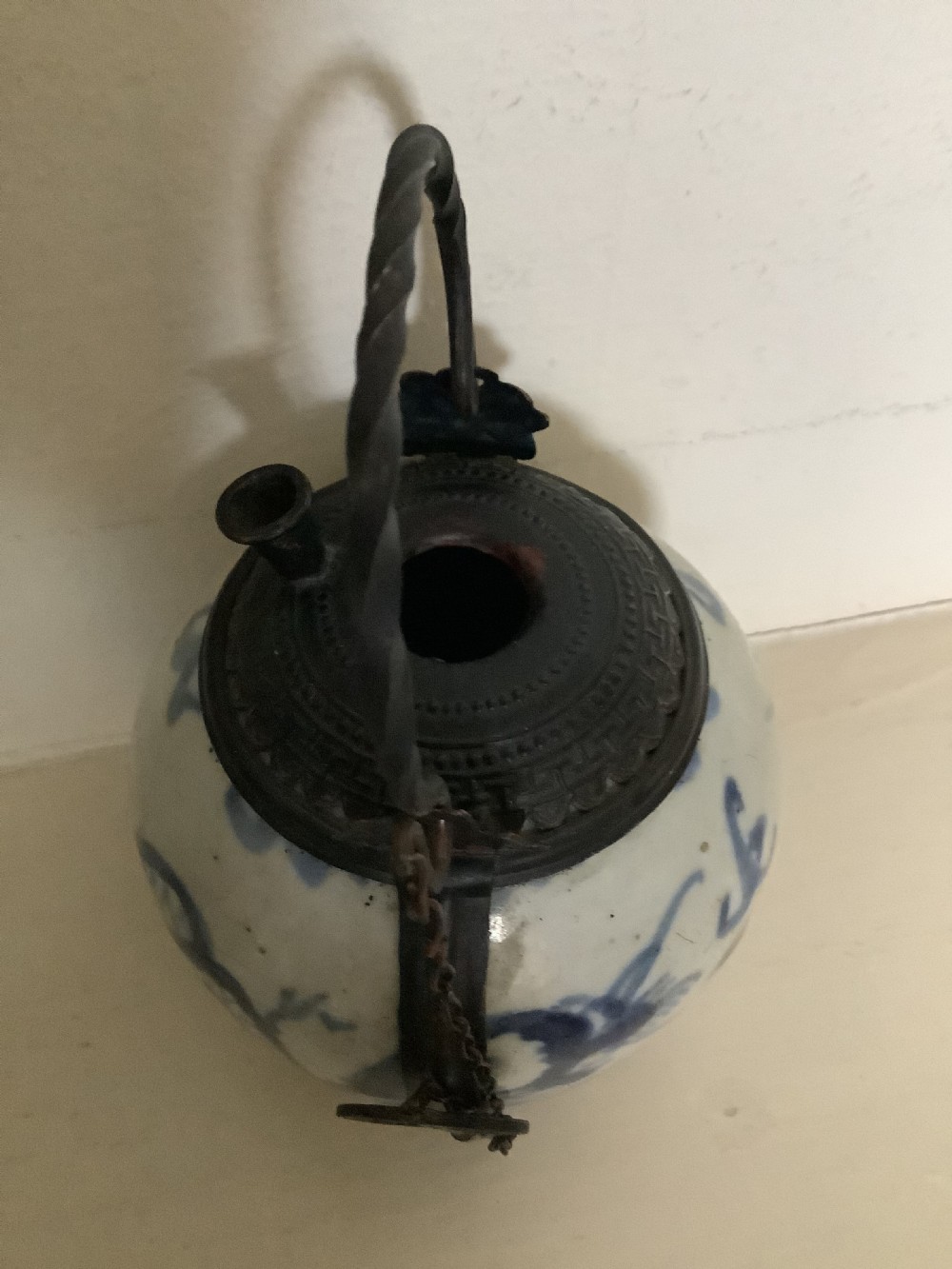A small 19th-century Chinese blue and white porcelain pot featuring hand-painted motifs, enclosed in metal wire mounts with an attached stopper and handle. View V