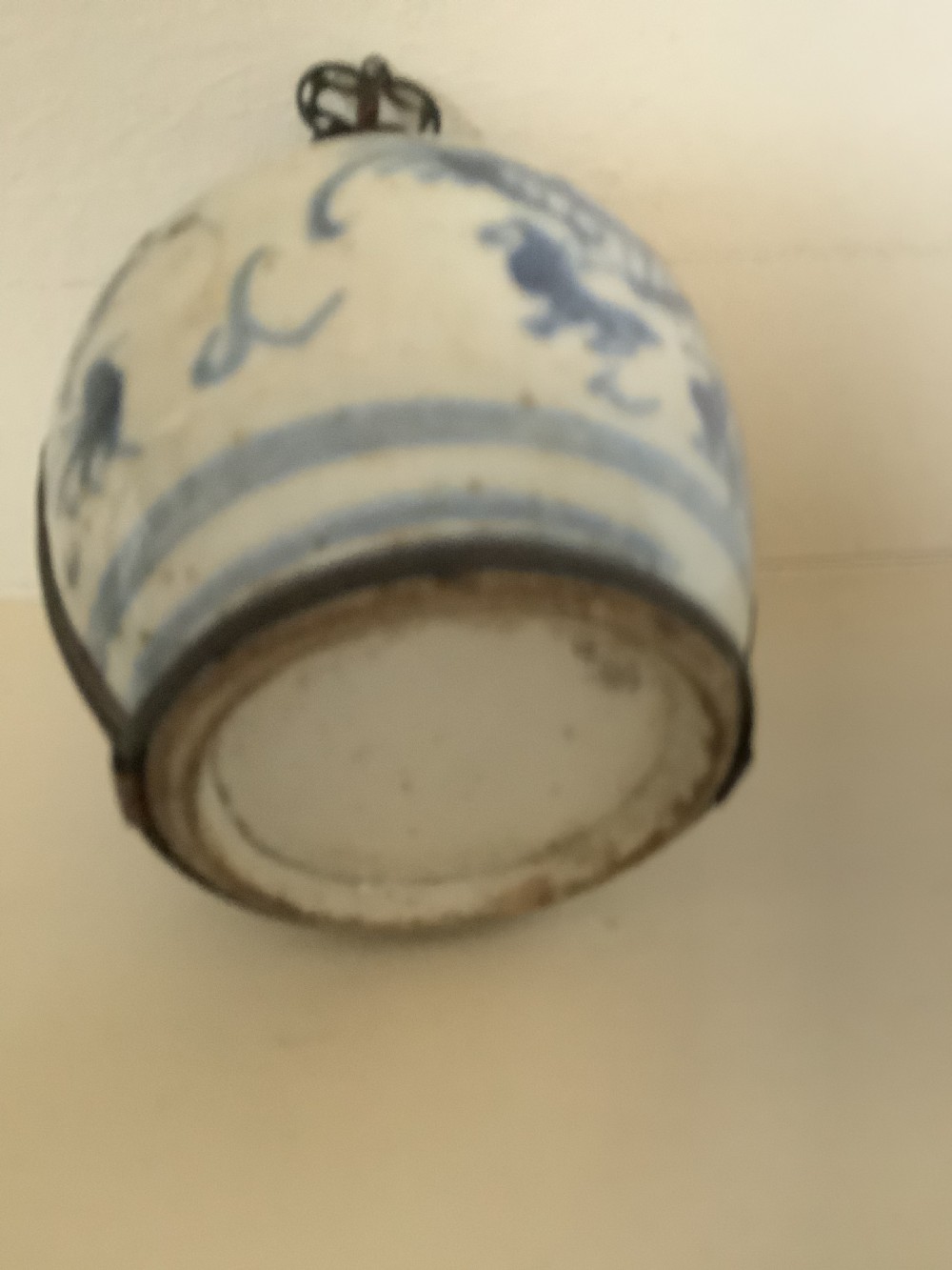A small 19th-century Chinese blue and white porcelain pot featuring hand-painted motifs, enclosed in metal wire mounts with an attached stopper and handle. View VI