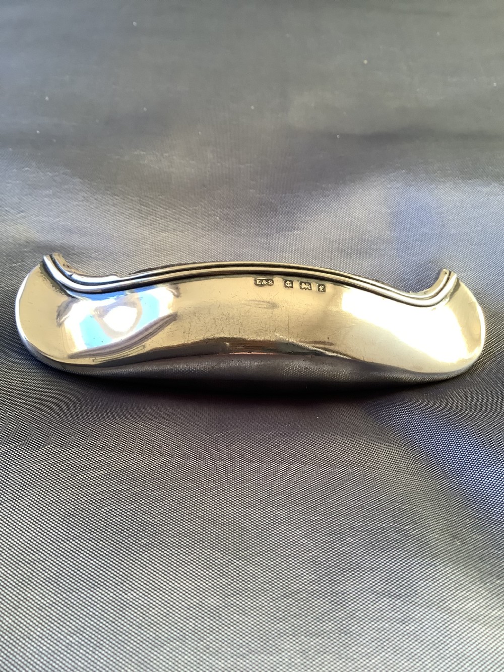 An Edwardian sterling silver pin cushion crafted in the form of a canoe with a dark fabric insert and visible hallmark stamps on the side. View VI