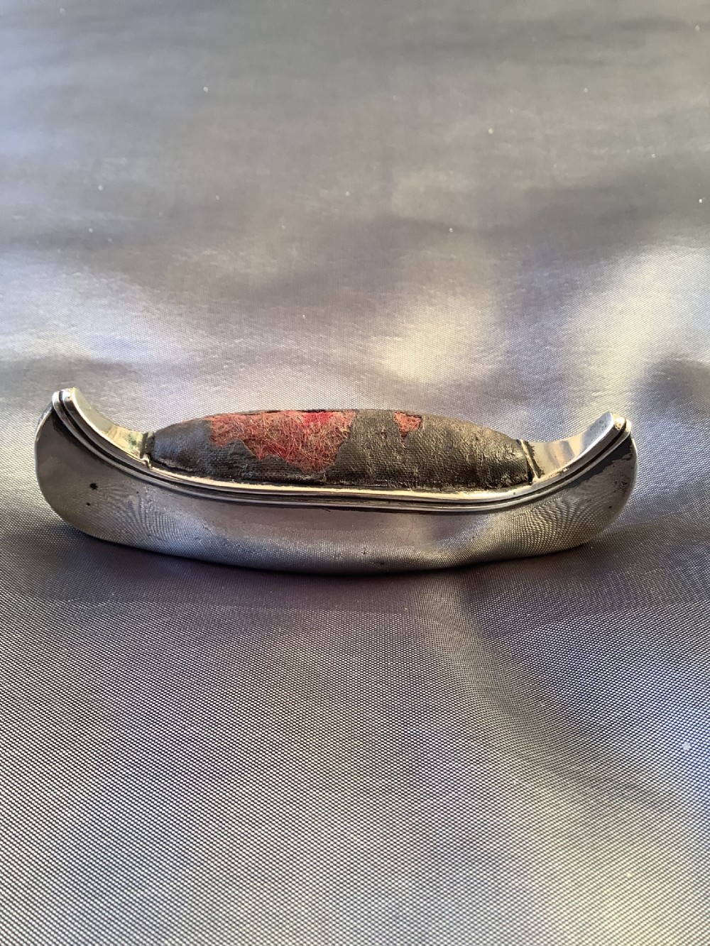 An Edwardian sterling silver pin cushion crafted in the form of a canoe with a dark fabric insert and visible hallmark stamps on the side. View II