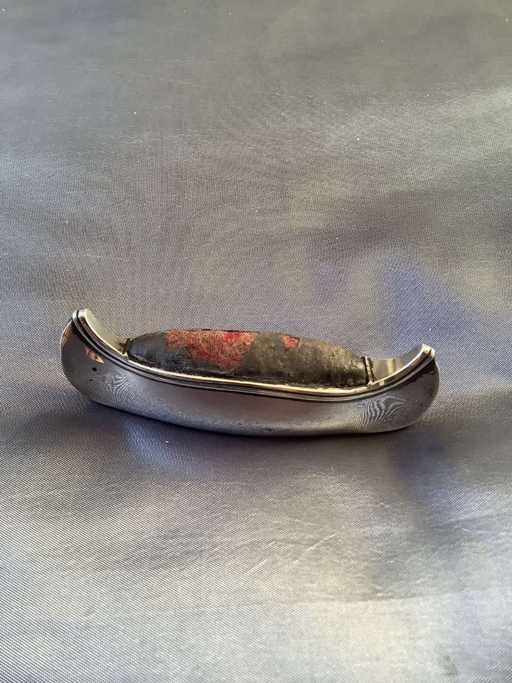 An Edwardian sterling silver pin cushion crafted in the form of a canoe with a dark fabric insert and visible hallmark stamps on the side. View V