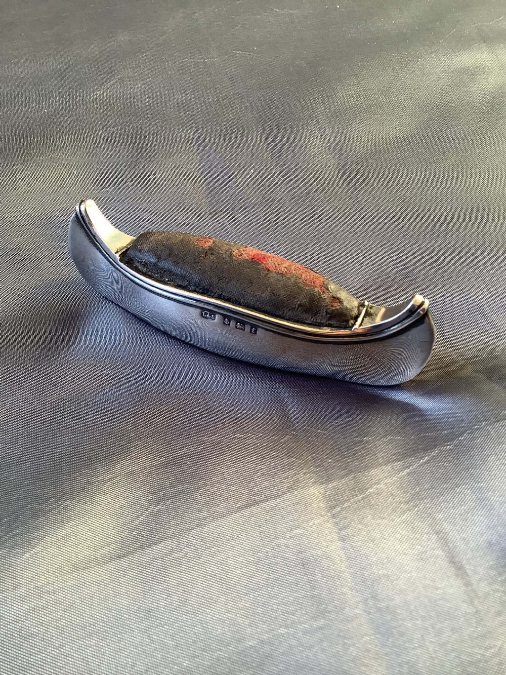 An Edwardian sterling silver pin cushion crafted in the form of a canoe with a dark fabric insert and visible hallmark stamps on the side.
