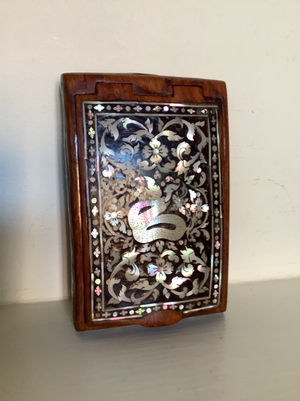 A rectangular dark hardwood box decorated with intricate mother-of-pearl inlay depicting a central serpent surrounded by floral scrolls and a geometric border. View III