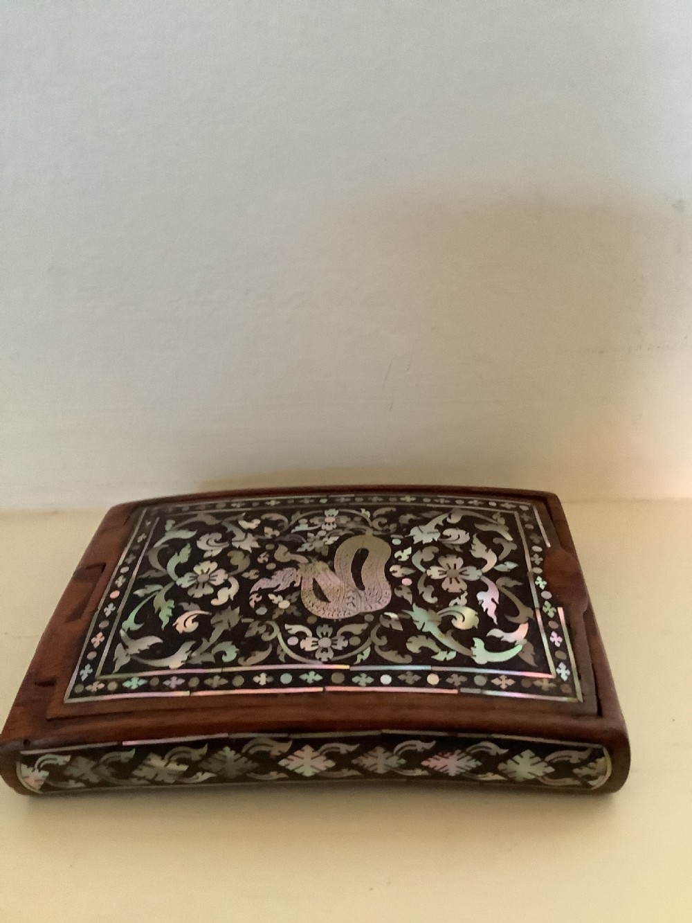 A rectangular dark hardwood box decorated with intricate mother-of-pearl inlay depicting a central serpent surrounded by floral scrolls and a geometric border. View II