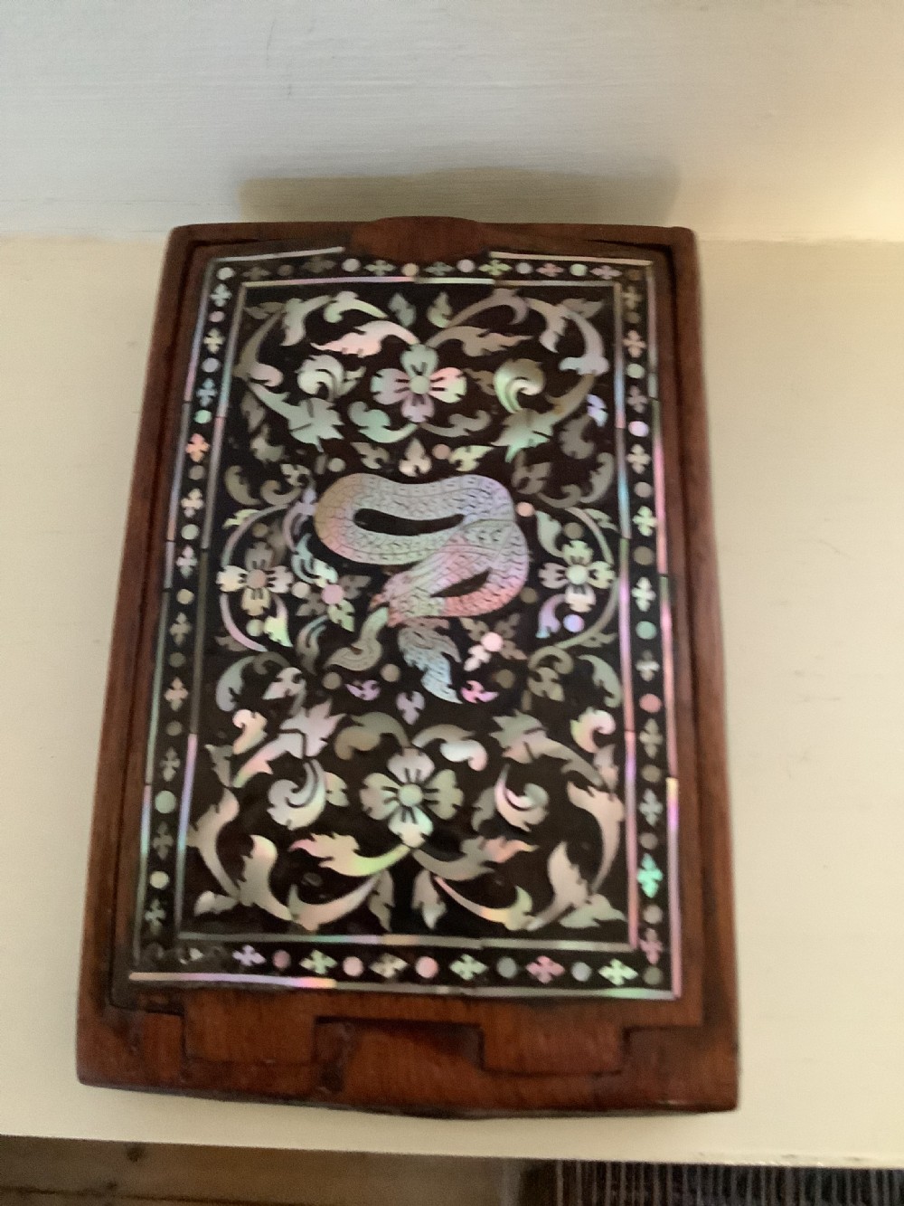 A rectangular dark hardwood box decorated with intricate mother-of-pearl inlay depicting a central serpent surrounded by floral scrolls and a geometric border.