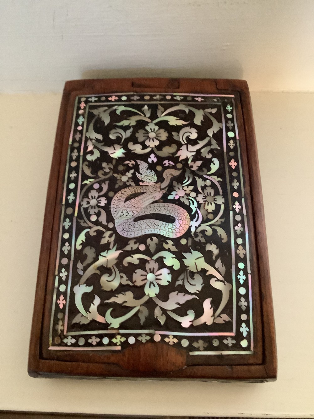 A rectangular dark hardwood box decorated with intricate mother-of-pearl inlay depicting a central serpent surrounded by floral scrolls and a geometric border. View IX