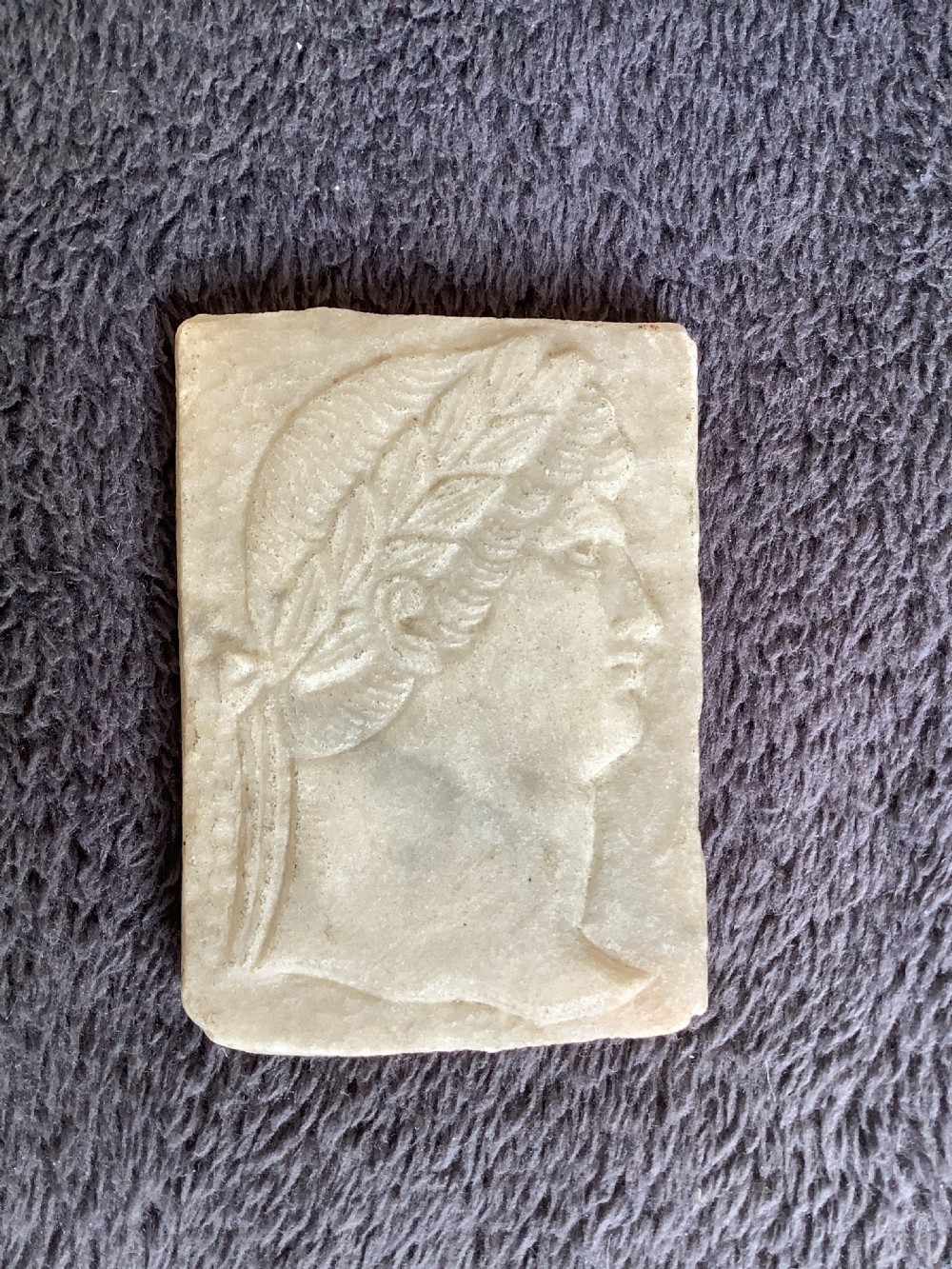 A rectangular carved marble plaque depicting the profile portrait of a Roman Emperor wearing a laurel wreath.