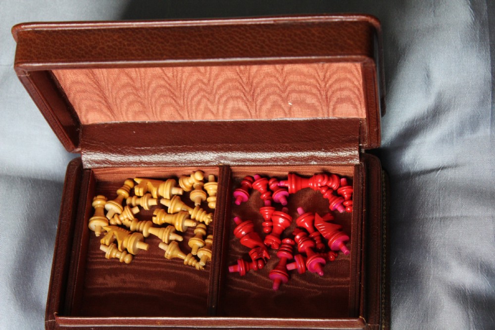 An antique miniature travelling chess set featuring a folding pegged board with alternating brown and cream squares beside a gilt-tooled brown leather case stamped Ajedrez. View III
