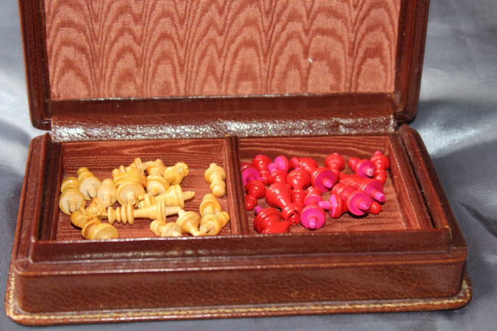 An antique miniature travelling chess set featuring a folding pegged board with alternating brown and cream squares beside a gilt-tooled brown leather case stamped Ajedrez. View VII