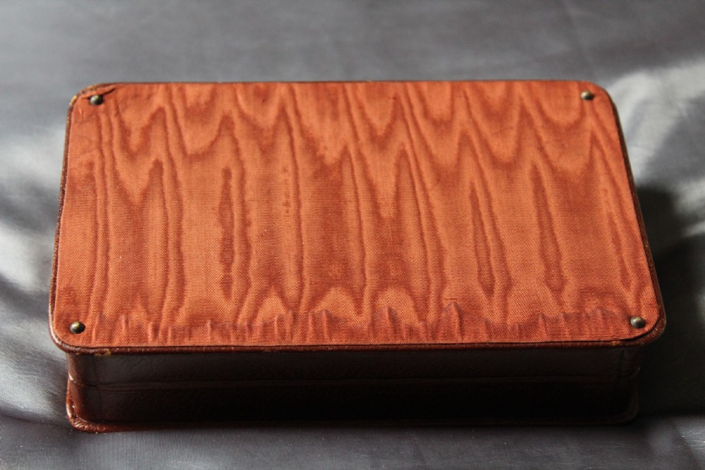An antique miniature travelling chess set featuring a folding pegged board with alternating brown and cream squares beside a gilt-tooled brown leather case stamped Ajedrez. View IX
