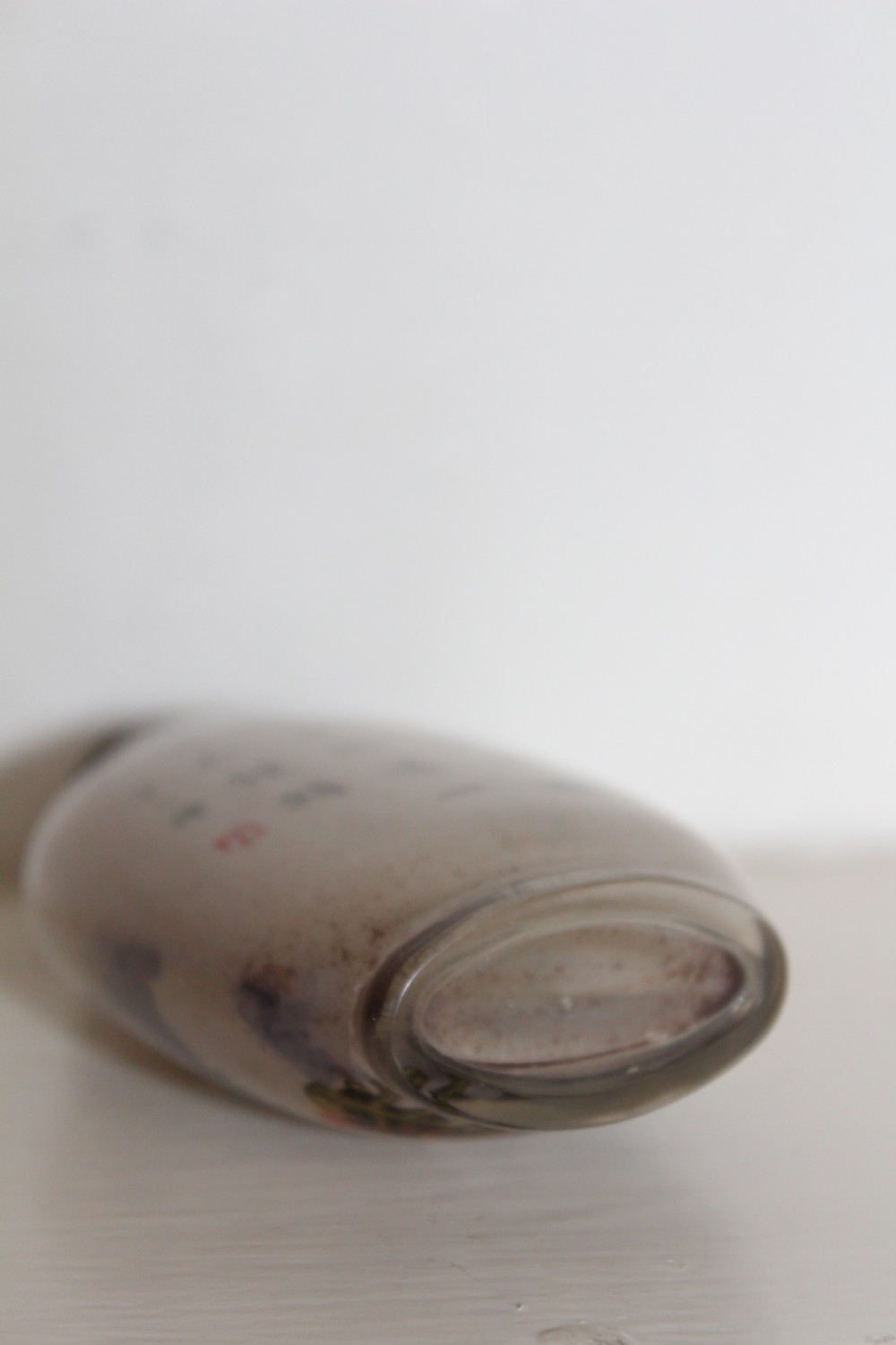 An inside-painted clear glass Chinese snuff bottle featuring detailed figures and calligraphy, topped with a rounded blue cabochon stopper. View V