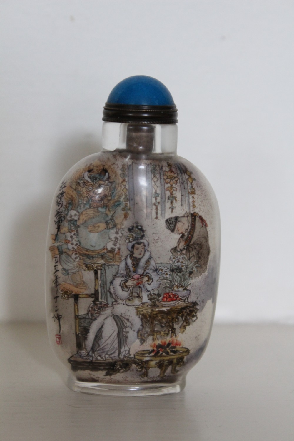An inside-painted clear glass Chinese snuff bottle featuring detailed figures and calligraphy, topped with a rounded blue cabochon stopper. View VIII