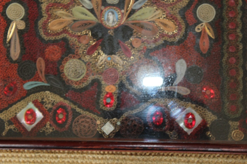 An antique framed 19th-century Indian quillwork picture featuring intricate red, black, and gold paper scrollwork embellished with beads and small painted portrait miniatures. View IV