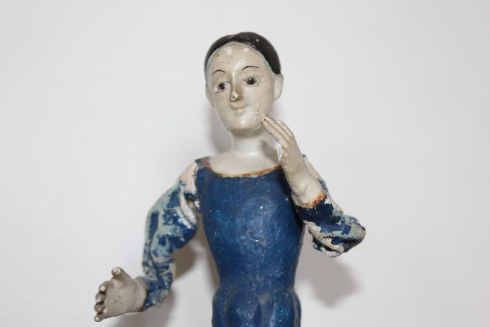 A pair of carved wooden folk art figures depicting a male and female figure dressed in blue gowns, mounted on rounded red scalloped bases. View II