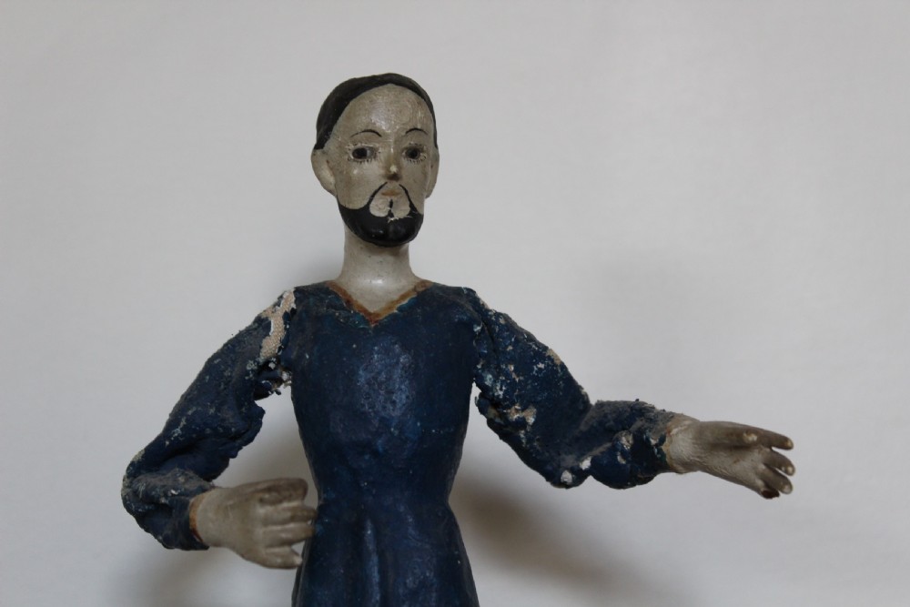A pair of carved wooden folk art figures depicting a male and female figure dressed in blue gowns, mounted on rounded red scalloped bases. View III