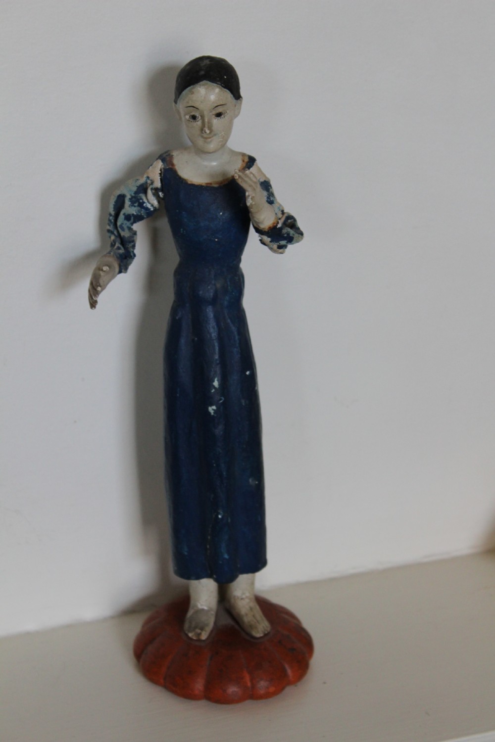 A pair of carved wooden folk art figures depicting a male and female figure dressed in blue gowns, mounted on rounded red scalloped bases. View VII