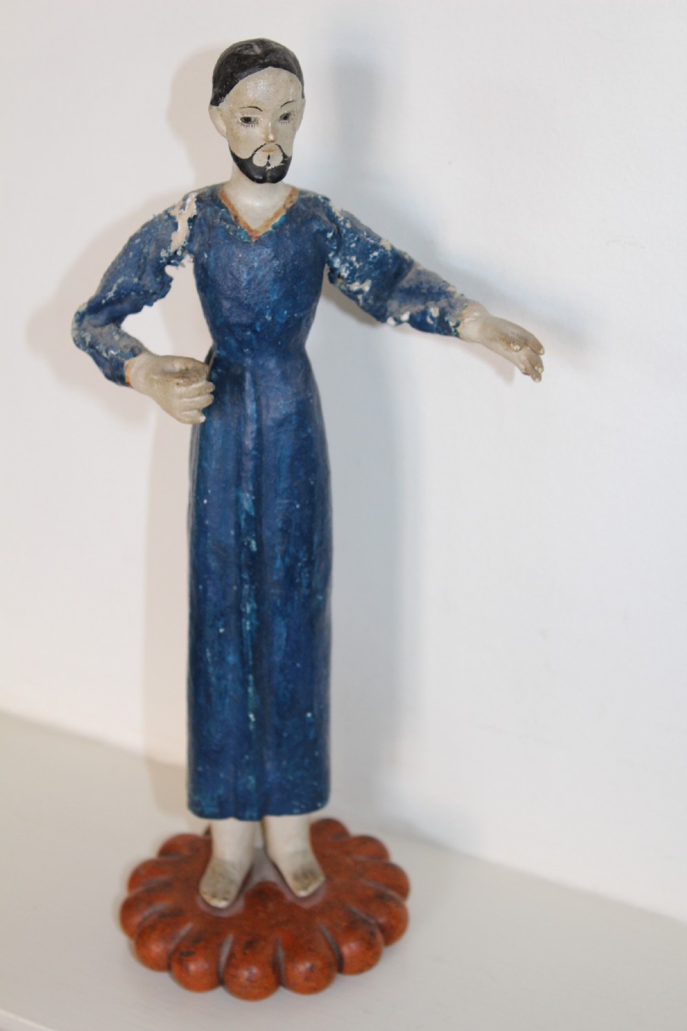 A pair of carved wooden folk art figures depicting a male and female figure dressed in blue gowns, mounted on rounded red scalloped bases. View VIII