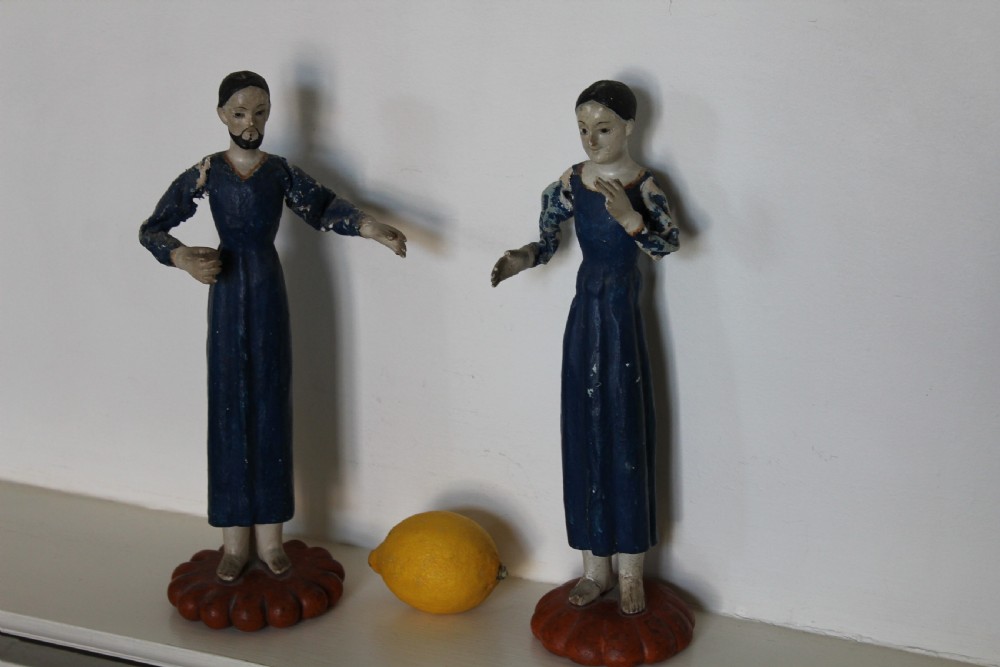 A pair of carved wooden folk art figures depicting a male and female figure dressed in blue gowns, mounted on rounded red scalloped bases. View IX