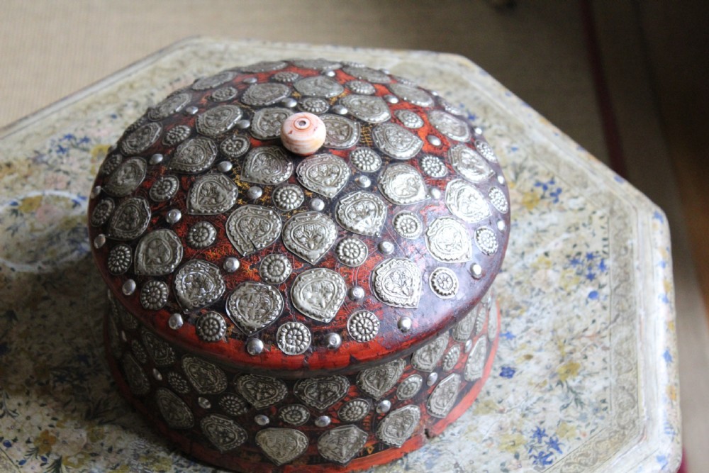 A circular red lacquered Kashmiri turban box with a domed lid, adorned with embossed silver-coloured metal mounts and a central turned knob. View II