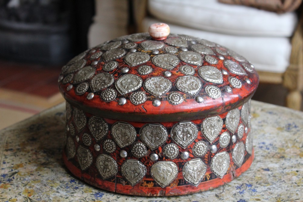A circular red lacquered Kashmiri turban box with a domed lid, adorned with embossed silver-coloured metal mounts and a central turned knob. View IV
